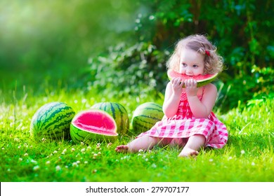 Child Eating Watermelon In The Garden. Kids Eat Fruit Outdoors. Healthy Snack For Children. Little Girl Playing In The Garden Holding A Slice Of Water Melon. Kid Gardening.