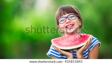 Child eating watermelon in garden. Pre teen girl with gasses and teeth braces. 