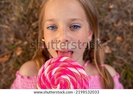 the child eats a bright lollipop. Beautiful girl model eats a bright lollipop. The child eats a big candy. Girl with huge pink candies. Girl with candy. Pink lollipop. Girl in panama and glasses. 