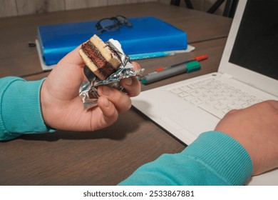 A child eats a cake while using a computer. Unhealthy diet in children - Powered by Shutterstock