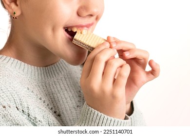 Child eats sweets, bites a waffle. Beautiful, plump lips, caucasian girl. Teeth with damaged enamel. Concept of sugar consumption, unhealthy food, pediatric dentistry, glucose. Close up.