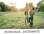 Child embrace parents happiness playing in green grass in park. Happy mother, father hug baby son walking in garden at sunset. Family spending time together outdoors. Children