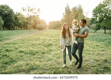 Child embrace parents happiness playing in green grass in park. Happy mother, father hug baby son walking in garden at sunset. Family spending time together outdoors. Children's day. Friendly family. - Powered by Shutterstock