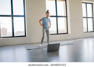 Child engaged in online learning while standing in a bright room with large windows
