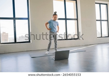 Child engaged in online learning while standing in a bright room with large windows