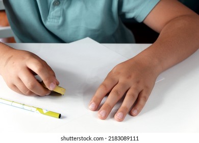 The Child Erases The Text On The White Paper With An Eraser.