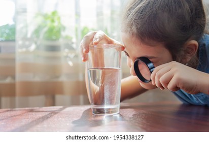 The child examines the water with a magnifying glass in a glass. Selective focus. Kid. - Shutterstock ID 1954338127