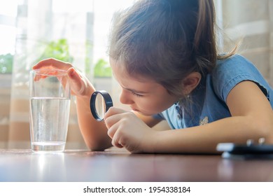 The child examines the water with a magnifying glass in a glass. Selective focus. Kid. - Powered by Shutterstock
