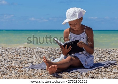 Child exploring a book while sitting on the seaside stones