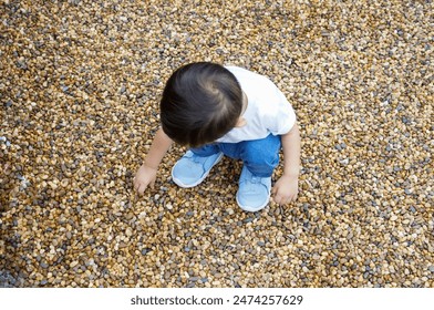 Child Exploring Pebbled Ground, Wearing White T-shirt and Blue Jean - Powered by Shutterstock