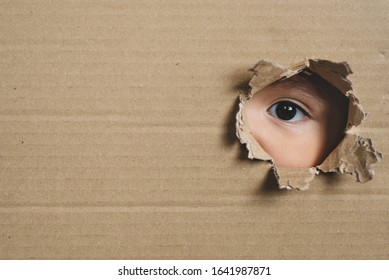 A Child Eye Looking Through A Hole On A Cardboard Box. Conept Of Spy And Stalker