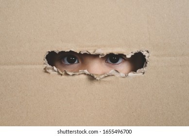 A Child Eye Looking Through A Hole On A Cardboard Box. Concept Of Spy And Stalker