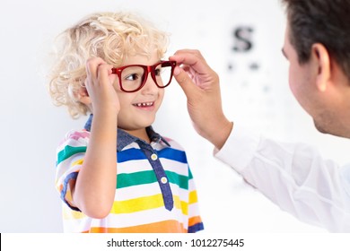 Child At Eye Sight Test. Little Kid Selecting Glasses At Optician Store. Eyesight Measurement For School Kids. Eye Wear For Children. Doctor Performing Eye Check. Boy With Spectacles At Letter Chart.