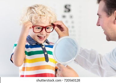 Child At Eye Sight Test. Little Kid Selecting Glasses At Optician Store. Eyesight Measurement For School Kids. Eye Wear For Children. Doctor Performing Eye Check. Boy With Spectacles At Letter Chart.