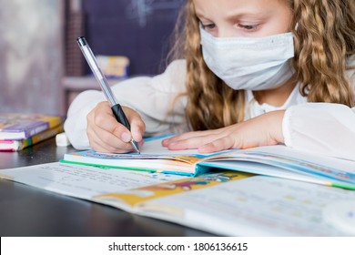 Child with face mask back at school after covid-19 quarantine and lockdown. Young elementary school girl with face protective mask writing in a book. Focus on pen. education concept. - Powered by Shutterstock