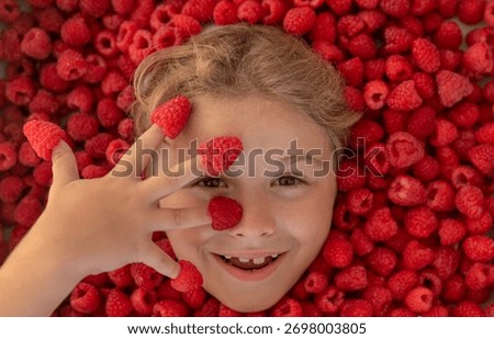 Child face with raspberry frame, close up raspberry background. Raspberries on fingers, summer banner.