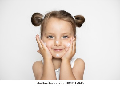 Child Face Skin Care And Protection, Cold Cream. Portrait Of Cute Little Caucasian 3 Years Old Girl, Applying Winter Cream, Posing On White Studio Background And Smiling