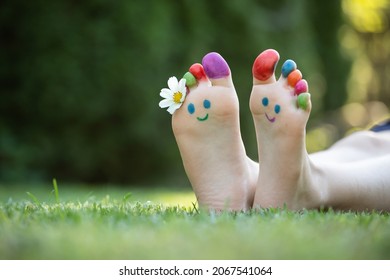 Child feet painted with colorful smiling face in green grass