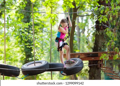 Child in forest adventure park. Kids climb on high rope trail. Agility and climbing outdoor amusement center for children. Little girl playing outdoors. School yard playground with rope way. - Powered by Shutterstock