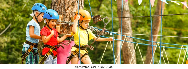 Child In Forest Adventure Park. Kids Climb On High Rope Trail. Agility And Climbing Outdoor Amusement Center For Children. Little Girl Playing Outdoors. School Yard Playground With Rope Way.