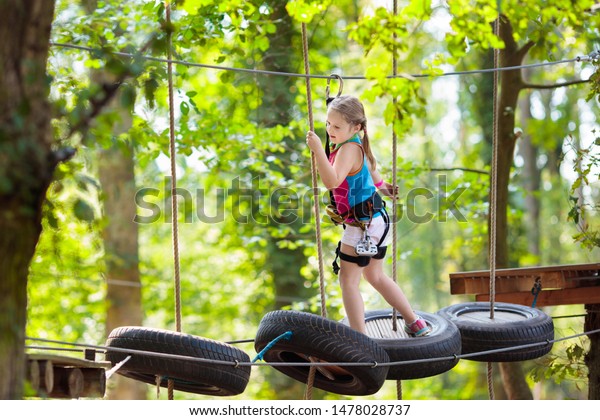 Child in forest adventure\
park. Kids climb on high rope trail. Agility amusement center. Zip\
line.