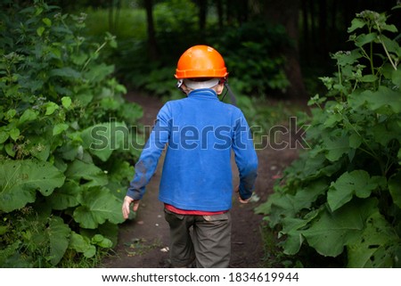 Child in the forest in an orange construction helmet. The boy's walk in an unknown place. Lost child in the mountains. The tourists forgot the boy.