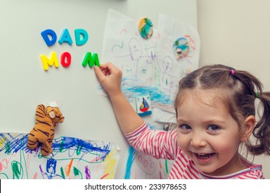 Child Forming Mom And Dad Words With Magnetic Letters On Refrigerator Door.