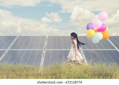 Child with future of alternative energy and sustainable energy. Funny kids holding colorful balloon running in meadow at Solar panel, photovoltaic. Eco-Friendly and Pure energy Concept