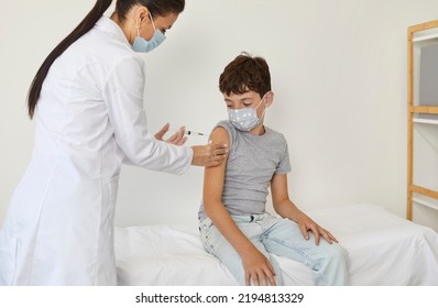 Child Getting Vaccine Injection For Covid, Flu, Monkeypox Or Other Infectious Disease. Nurse Or Doctor Giving Shot To School Kid Who Sitting On Couch In Medical Office. Children's Vaccination