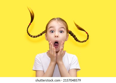 A child girl with an amazed and shocked look and pigtails thrown up in the top on a yellow background. The child shows wild emotions and looks in amazement. Funny girl on yellow background