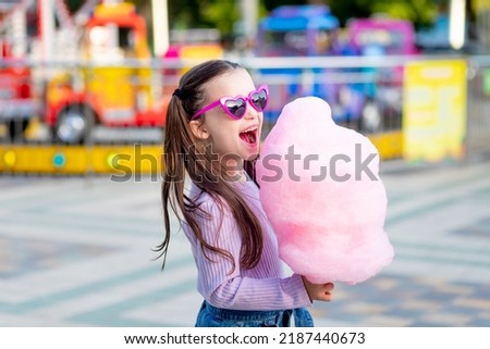 a child girl in an amusement park in the summer eats cotton candy near the carousels in sunglasses, the concept of summer holidays and school holidays