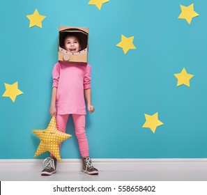 Child girl in an astronaut costume is playing and dreaming of becoming a spacemen. Portrait of funny kid on a background of bright blue wall with yellow stars.