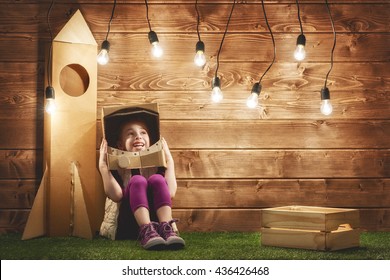 Child Girl In An Astronaut Costume With Toy Rocket Playing And Dreaming Of Becoming A Spacemen.