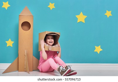 Child girl in an astronaut costume with toy rocket playing and dreaming of becoming a spacemen. Portrait of funny kid on a background of bright blue wall with yellow stars.