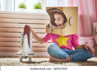 Child girl in an astronaut costume with toy rocket playing and dreaming of becoming a spacemen. Portrait of funny kid near windows.