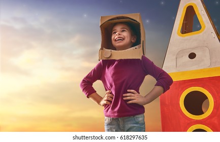 Child girl in astronaut costume with toy rocket playing and dreaming of becoming a spacemen. Portrait of funny kid on a background of sunset star sky on nature. Family games outdoors.