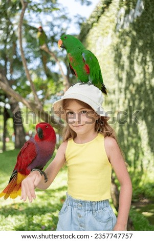 child girl with beautiful macaw parrot in her shoulder in the zoo, Bali, Indonesia. 
