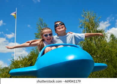 Child Girl And Boy Fly On Blue Plane Attraction In City Park, Happy Childhood, Summer Vacation Concept