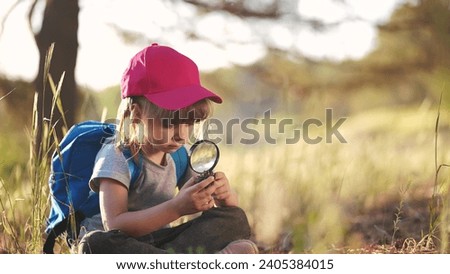 child girl boy scout studying pine cone in the forest with a magnifying glass. happy family child lifestyle dream concept. child tourist explorer with magnifying glass in the forest