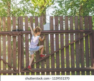 a child, a girl climbs a wooden fence in the village - Powered by Shutterstock