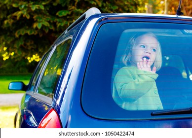 Child Girl Closed Alone In The Back Of A Parking Car On A Hot Day. Concept Image Of Danger Of Overheating In Car For Young Children In The Summer