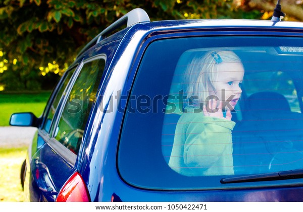 Child girl closed in the back of a car on a hot\
day. Concept image of danger of overheating in car for young\
children in the summer