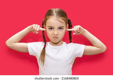 Child girl covers her ears with her hands and gets angry. A little girl with pigtails is outraged by loud sounds and closes her ears. Portrait of a cute baby on a red background