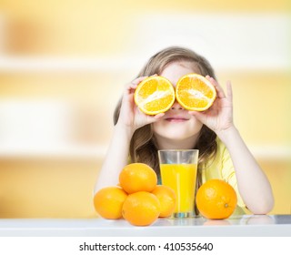 Child Girl Drinking Glass Of Fresh Orange Juice Indoors.Healthy Lifestyle.Kid Sitting Home At Table Eating Oranges Background Empty Copy Space.