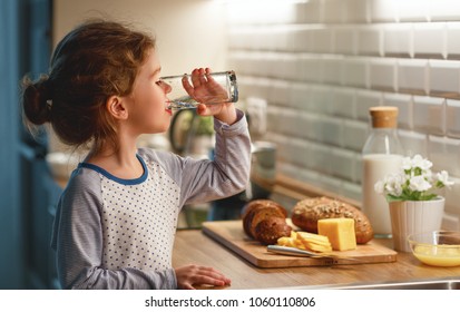 child girl is drinking water in the kitchen at home