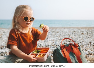 Child Girl Eating Broccoli With Lunch Box Picnic On Beach Vegan Healthy Food Travel Lifestyle Outdoor Summer Vacations Kid With Backpack And Lunchbox 