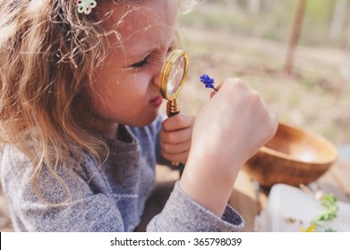 Child Girl Exploring Nature In Early Spring, Looking At First Sprouts With Loupe. Teaching Kids To Love Nature.