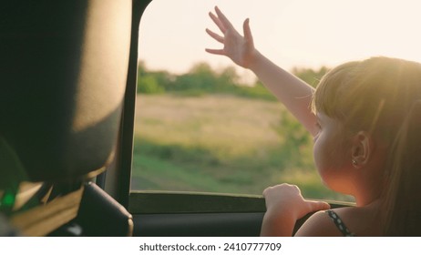 child girl face looks smiling from car out window, sun glare sunset, happy girl smiling from car window, enjoying travel, teenage girl waving her hand car window, active lifestyle, success concept