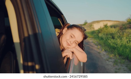 child girl face looks smiling from car out window, bright light setting sun through his fingers, girl hand sun, free young girl, car, child sitting child car seat, active, catches wind with his hand