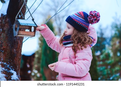 Child Girl Feeding Birds In Winter. Bird Feeder In Snowy Garden, Helping Birds During Cold Season, Teaching Kids To Love And Protect Nature